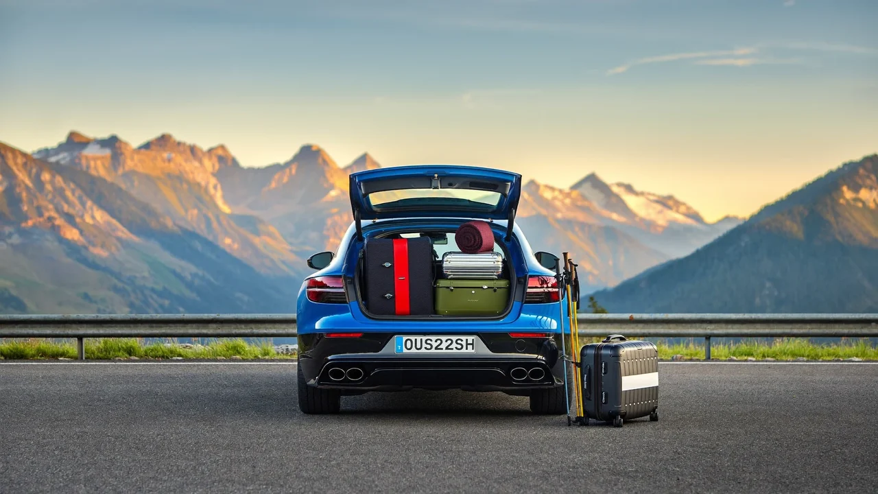 Gepacktes Auto an einem Alpen-Rastplatz im Morgengrauen, Kofferraum offen, Berge im Dunst